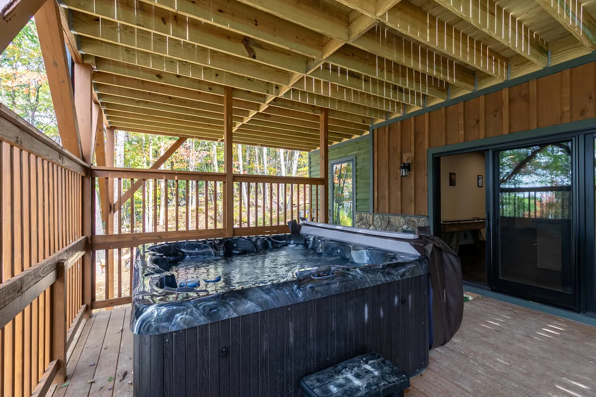A serene interior space featuring a hot tub under wooden beams, with an inviting outdoor view. The atmosphere is tranquil, blending indoor comfort with the beauty of nature just outside.