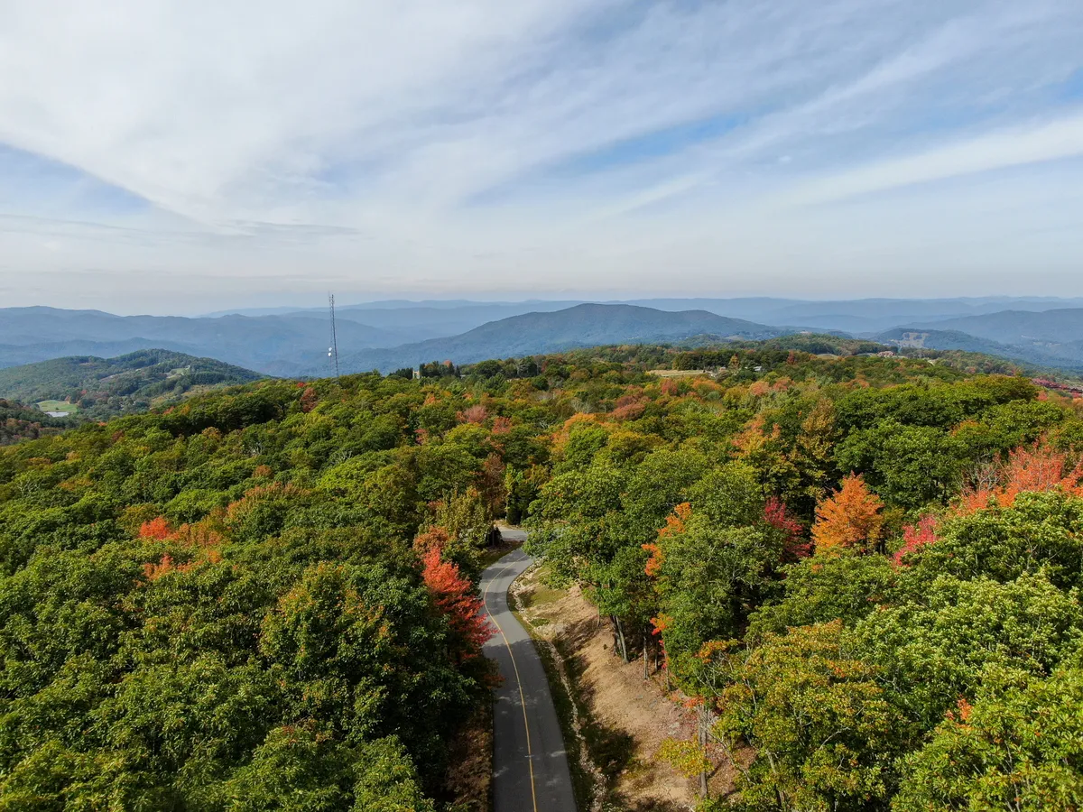 A stunning panoramic view of a winding road framed by colorful trees and rolling mountains in the distance. This expansive vista embodies the natural splendor of the region and evokes a sense of adventure and exploration just beyond the doorstep.