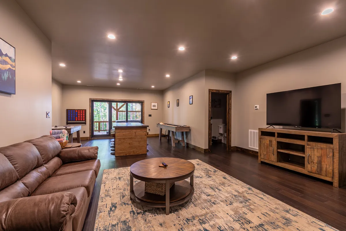 An inviting interior space featuring a sofa, coffee table, television, and a pool table near a window with a lovely view. The room is perfect for socializing, playing games, and unwinding with family on rainy days or quiet evenings at home.