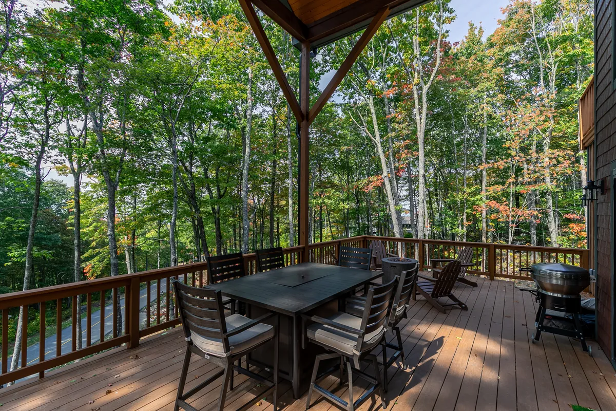 An outdoor dining area is depicted with a large table surrounded by trees, offering comfortable seating in a tranquil natural setting. The space exudes a sense of relaxation and togetherness for outdoor meals or morning coffee.