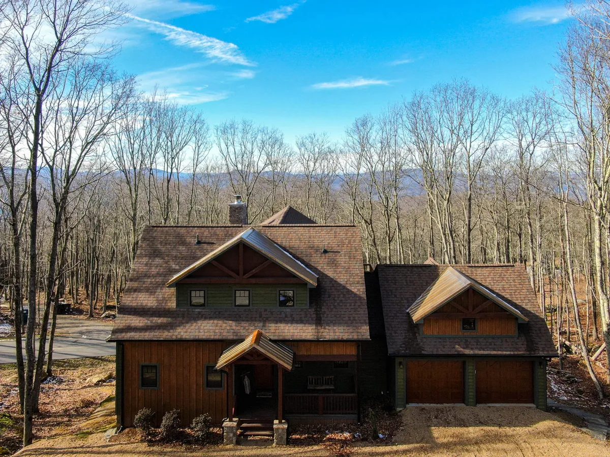 The image showcases a charming cabin nestled among towering trees, with stunning mountain views in the background. The spacious porch faces the sunset, inviting guests to relax and soak in the natural beauty. The peaceful surroundings evoke a sense of tranquility and outdoor adventure, perfect for gatherings and quiet moments alike.