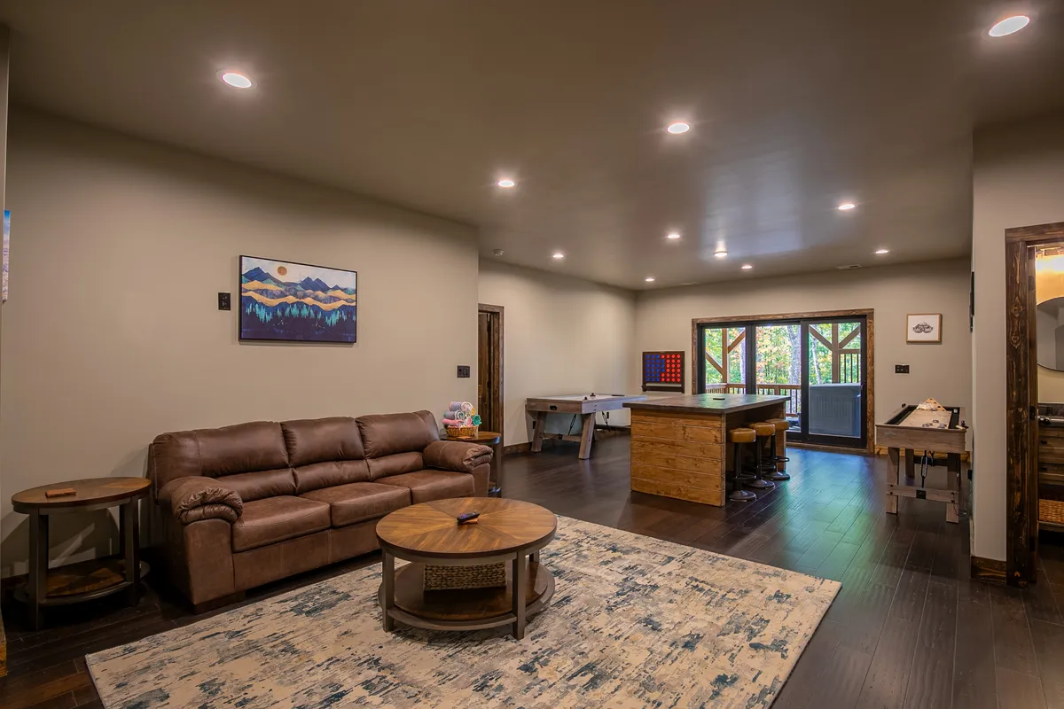 A comfortable lounge area with a leather sofa, wooden game tables, and large windows offering views of the outdoors. Decorative wall art adds a cozy touch, while the presence of games reinforces the room's purpose as a recreational hub.